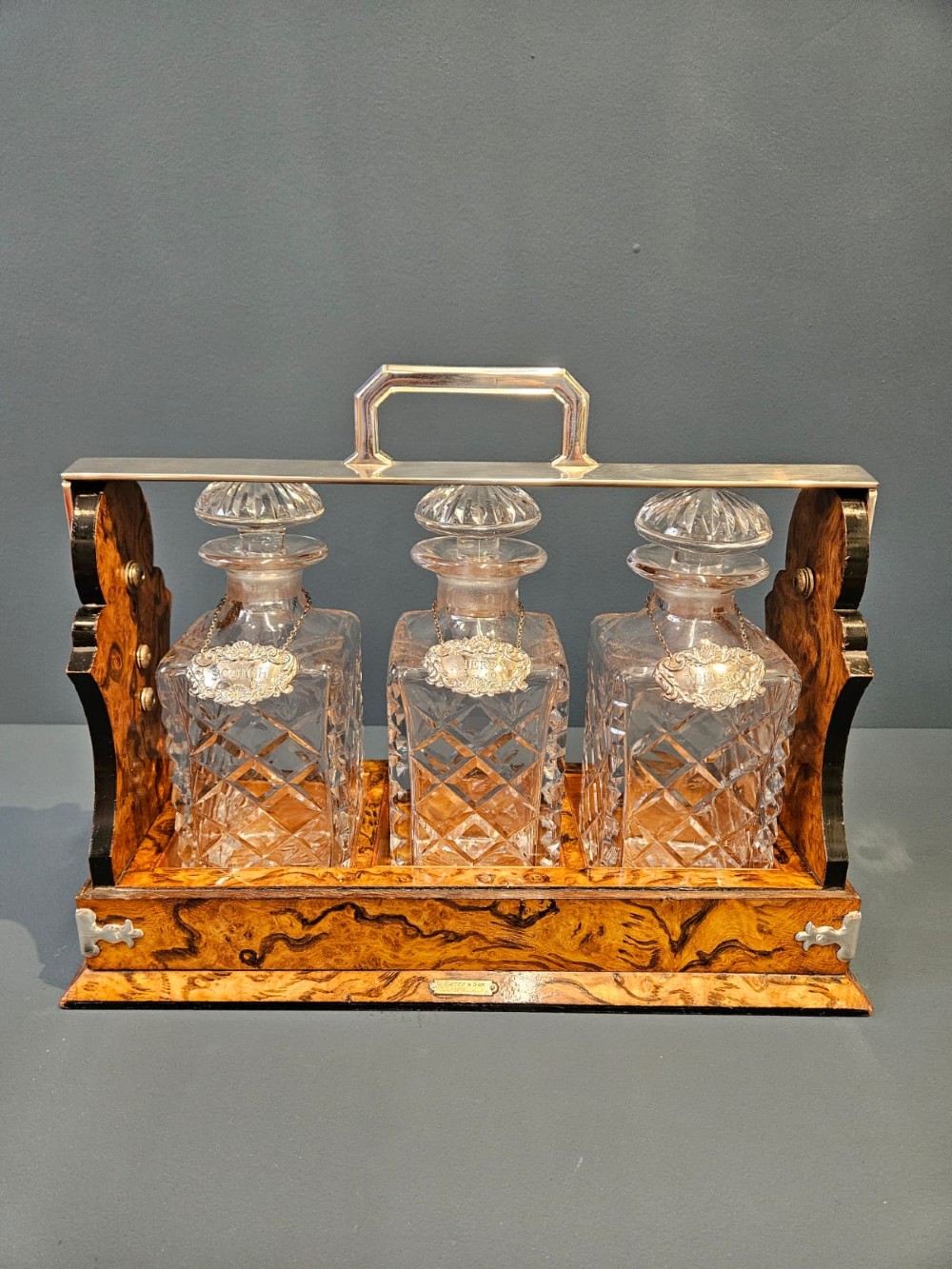 A Victorian burr walnut tantalus with a silver-plated handle and locking frame securing three cut glass decanters with silver labels. View II