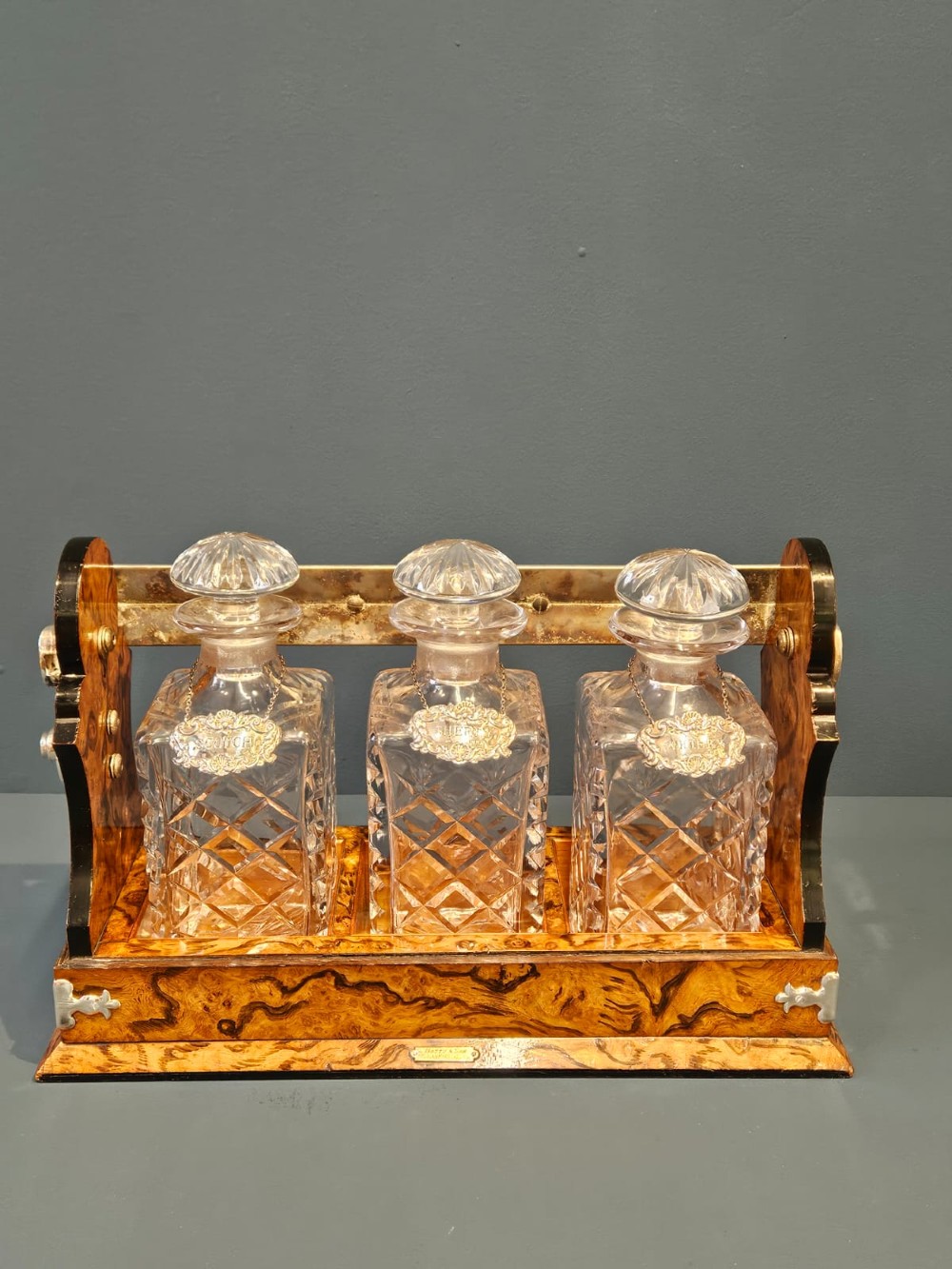 A Victorian burr walnut tantalus with a silver-plated handle and locking frame securing three cut glass decanters with silver labels. View V