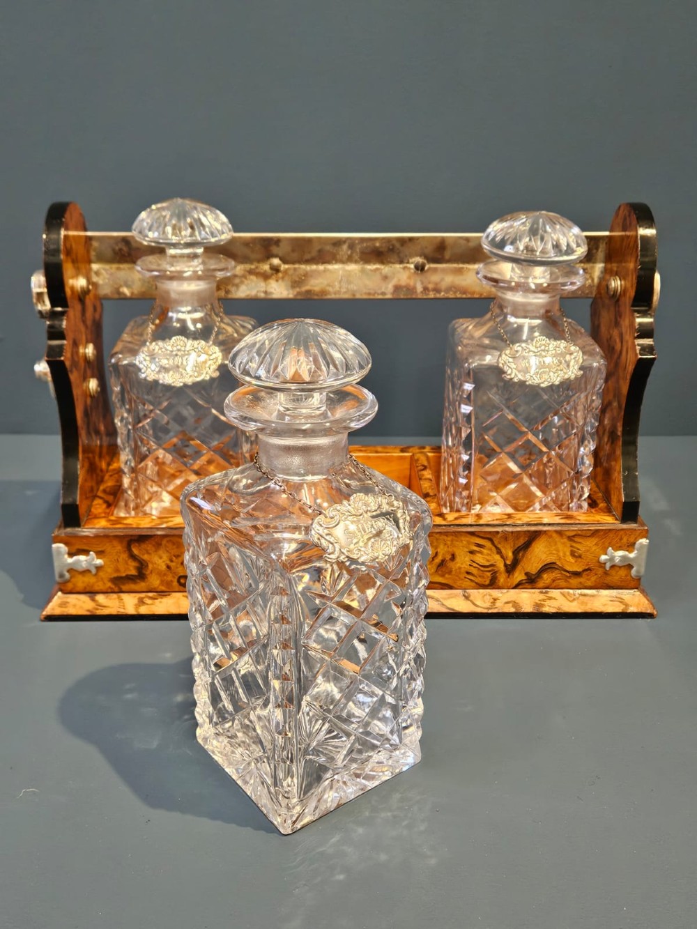 A Victorian burr walnut tantalus with a silver-plated handle and locking frame securing three cut glass decanters with silver labels. View VI