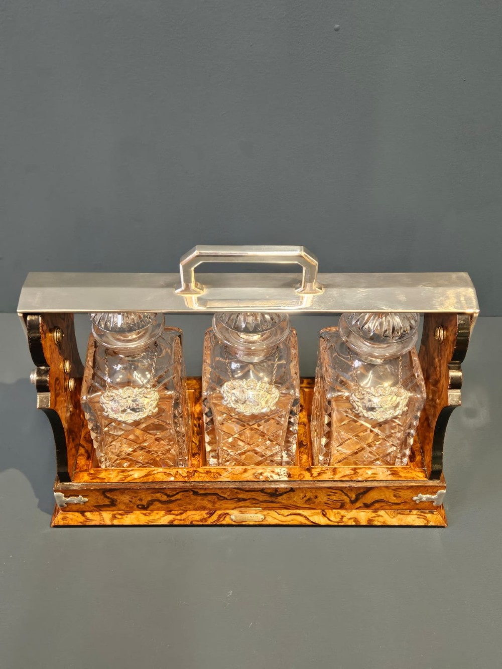 A Victorian burr walnut tantalus with a silver-plated handle and locking frame securing three cut glass decanters with silver labels. View VII