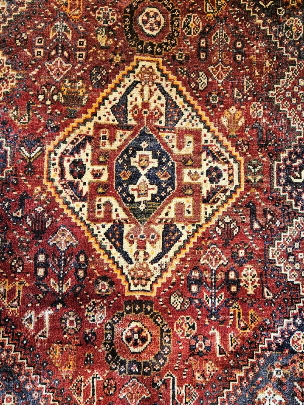 A rectangular hand-knotted Persian rug featuring a rust-red field with a central diamond medallion, navy blue accents, and a detailed multi-tiered floral border. View V