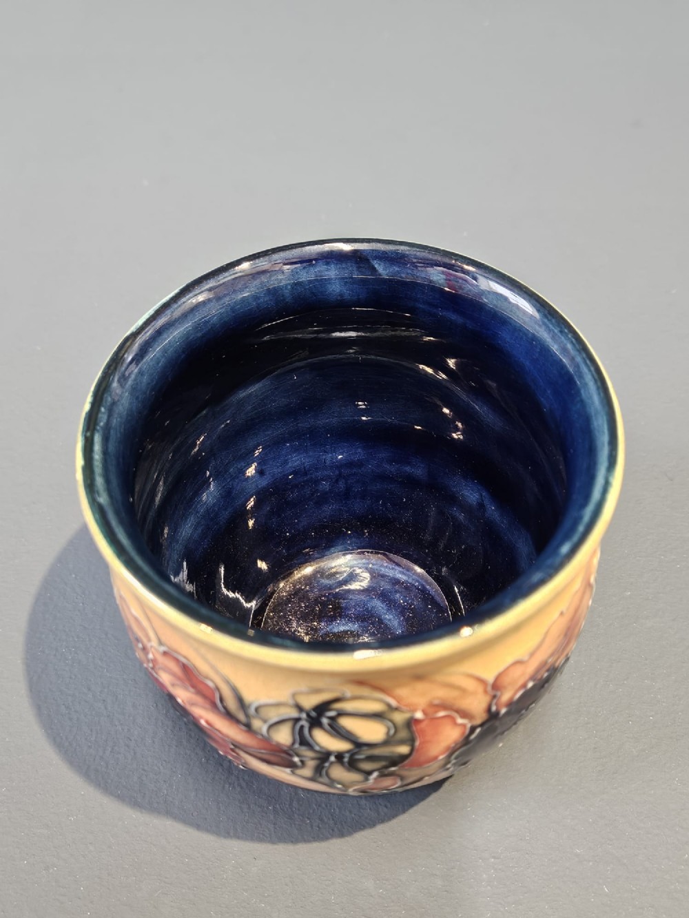 A rounded glazed ceramic vase featuring a yellow upper section decorated with tubelined orchids above a dark cobalt blue base. View V