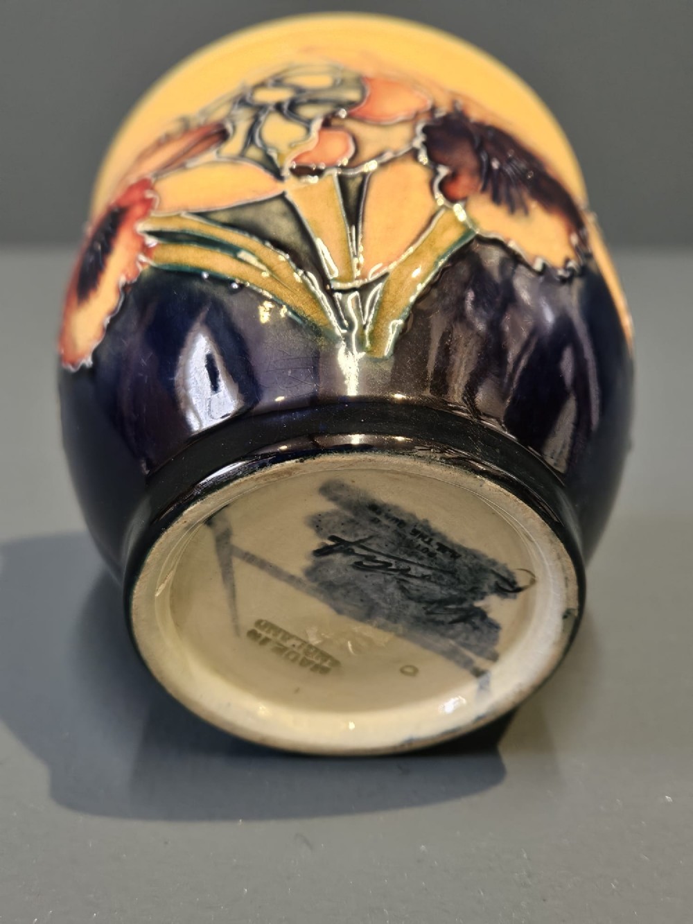A rounded glazed ceramic vase featuring a yellow upper section decorated with tubelined orchids above a dark cobalt blue base. View VI