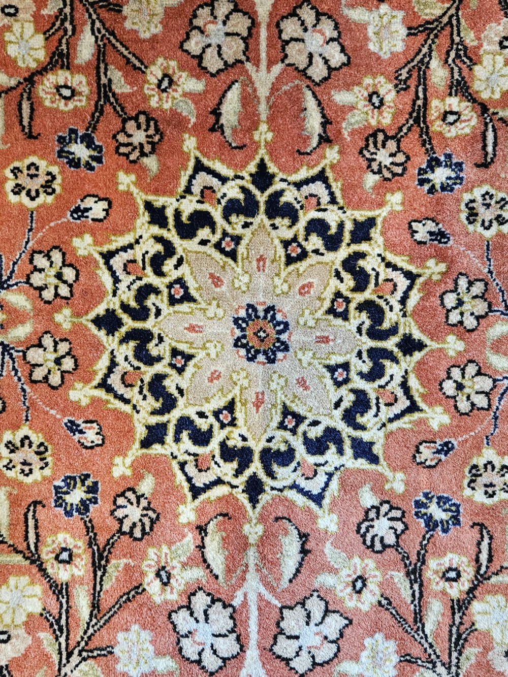 A rectangular pure wool hearth rug with a central floral medallion, salmon terracotta ground, and navy blue patterned borders. View II