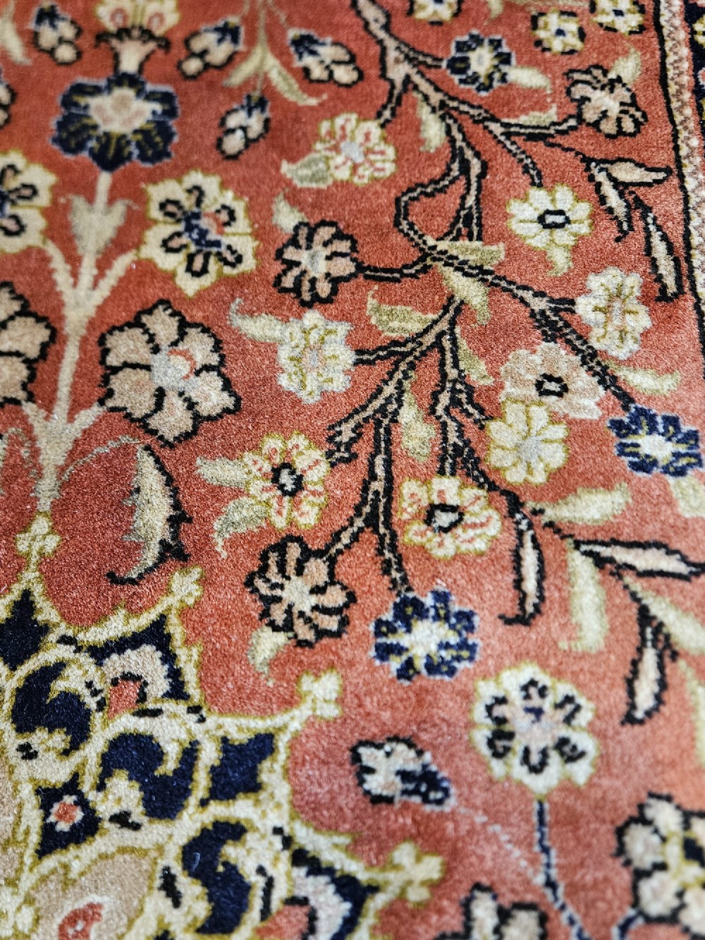 A rectangular pure wool hearth rug with a central floral medallion, salmon terracotta ground, and navy blue patterned borders. View VI