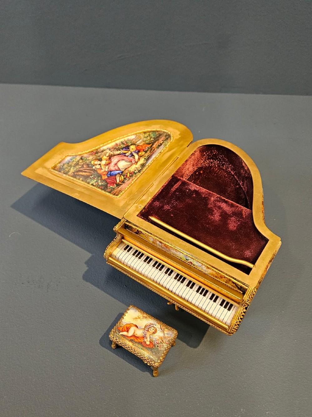 A miniature grand piano and matching stool music box crafted from gilt metal with hand-painted enamel panels depicting classical figures. View II