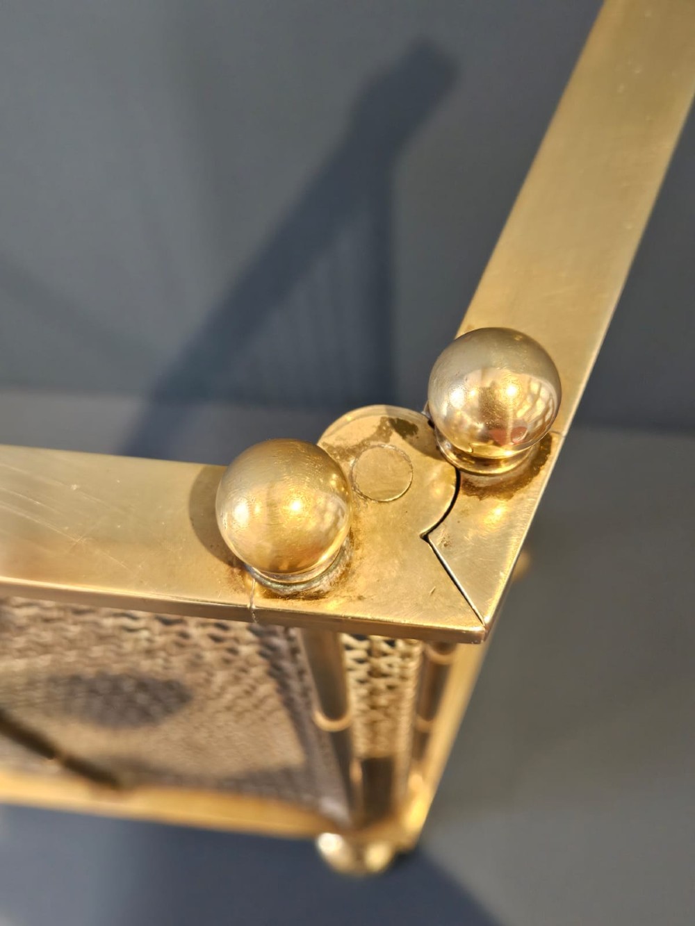A Victorian cast brass fire guard featuring a woven wire mesh screen, turned brass finials, a central carrying handle, and small turned brass feet. View V