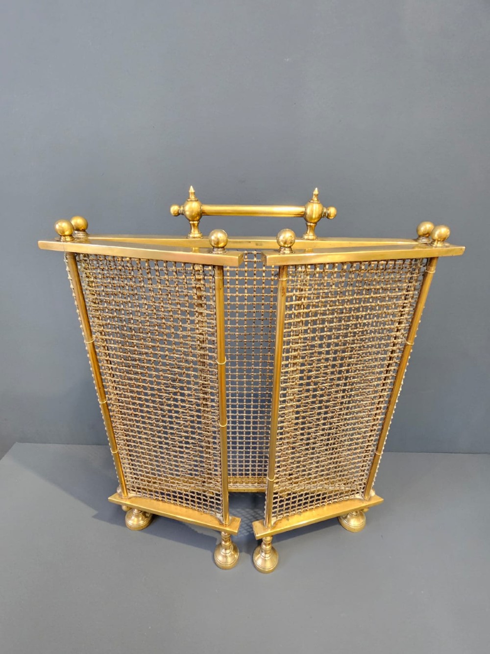 A Victorian cast brass fire guard featuring a woven wire mesh screen, turned brass finials, a central carrying handle, and small turned brass feet. View VIII