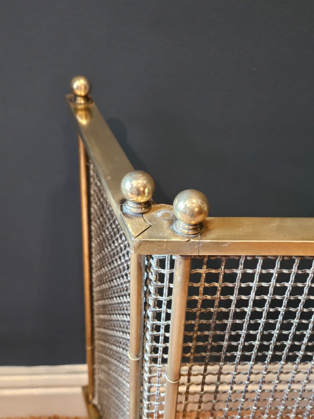 A Victorian cast brass fire guard featuring a woven wire mesh screen, turned brass finials, a central carrying handle, and small turned brass feet. View IX