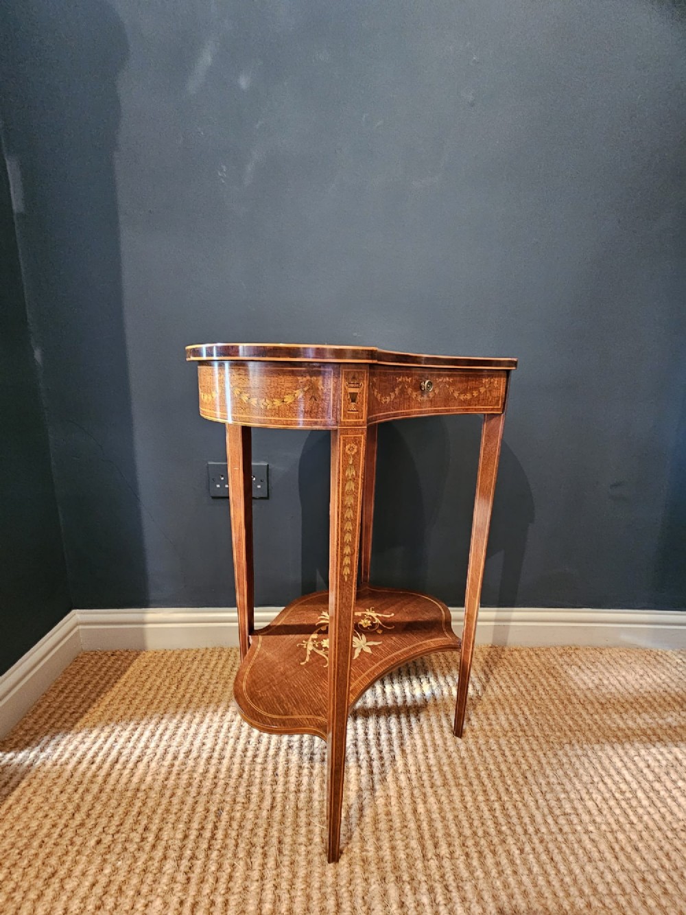 An Edwardian kidney-shaped mahogany occasional table featuring classical marquetry inlay, a single drawer, and an undertier shelf supported by slender tapered legs. View VI