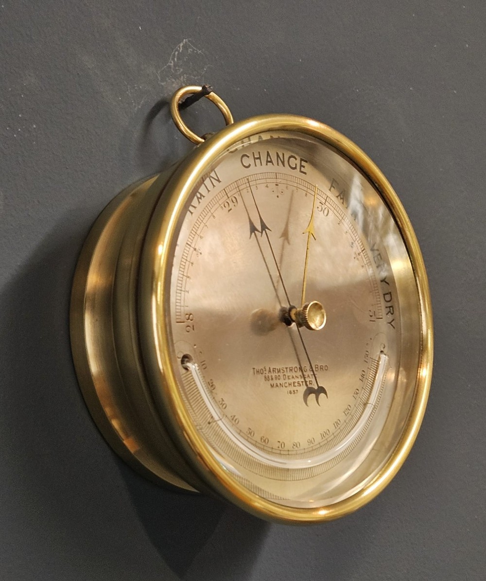 A circular Victorian brass aneroid barometer featuring an engraved silvered dial with weather scale, integrated thermometer, and a top suspension ring. View II