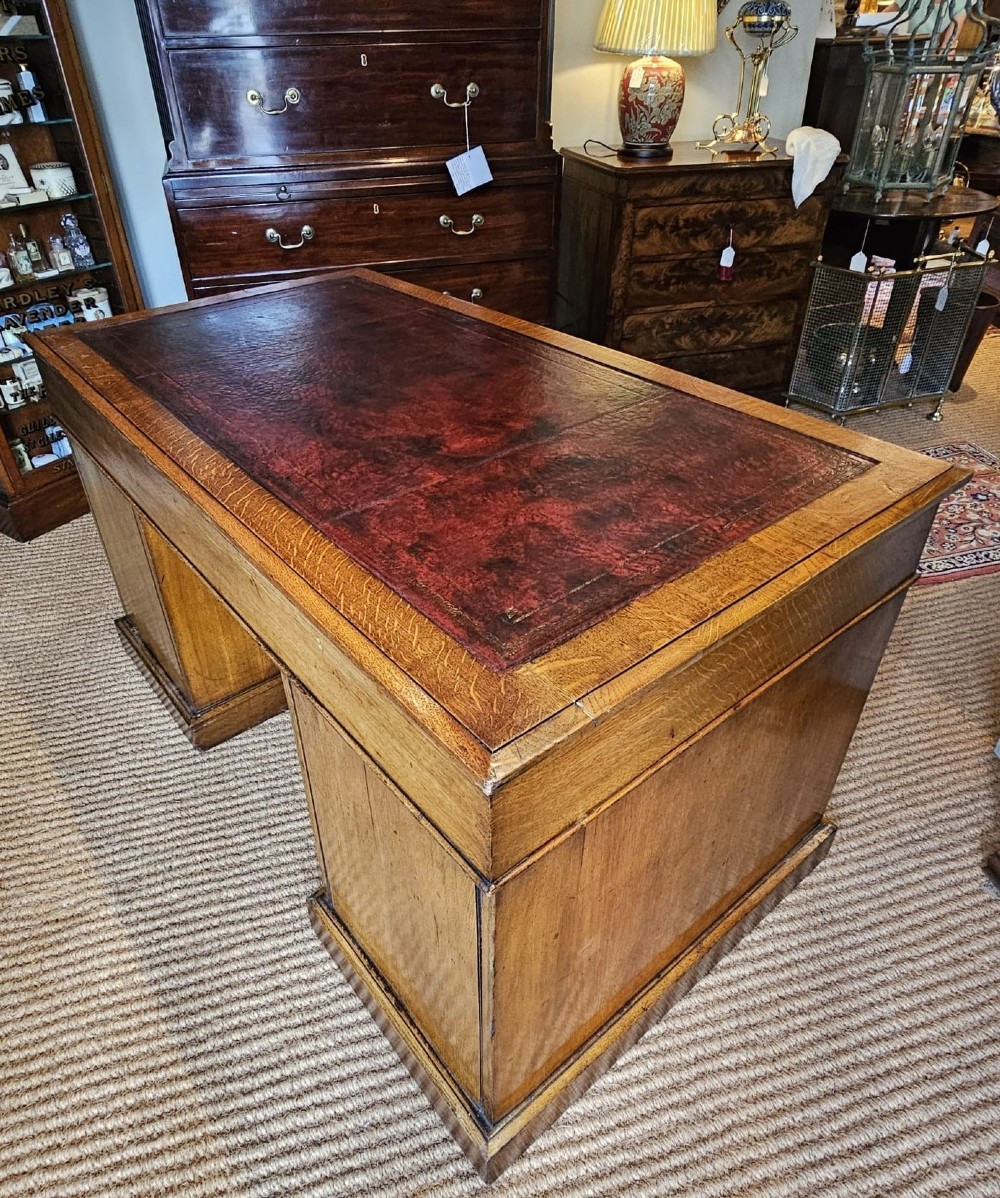 A Victorian oak pedestal desk featuring a red leather inset top, brass swing handles, and twin pedestals housing multiple drawers. View V