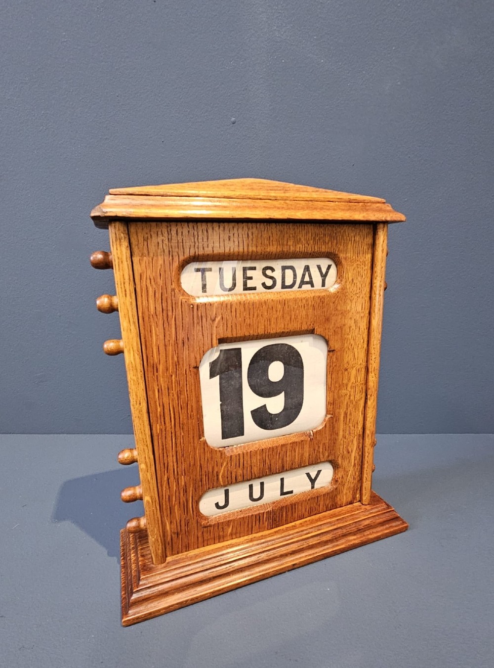A late Victorian figured oak perpetual desk calendar with turned side knobs and three apertures displaying the day, date, and month. View II