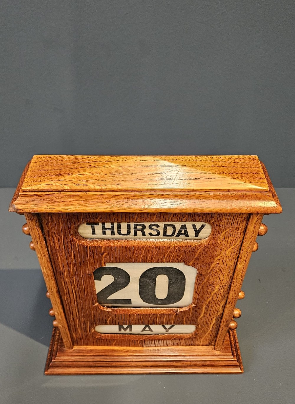 A late Victorian figured oak perpetual desk calendar with turned side knobs and three apertures displaying the day, date, and month. View VIII