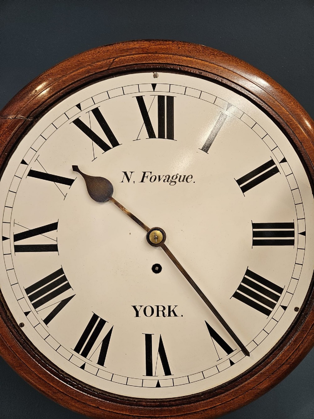 A round late Victorian mahogany wall clock featuring a brass bezel, white painted dial with black Roman numerals, and signature reading N. Fovague York. View V