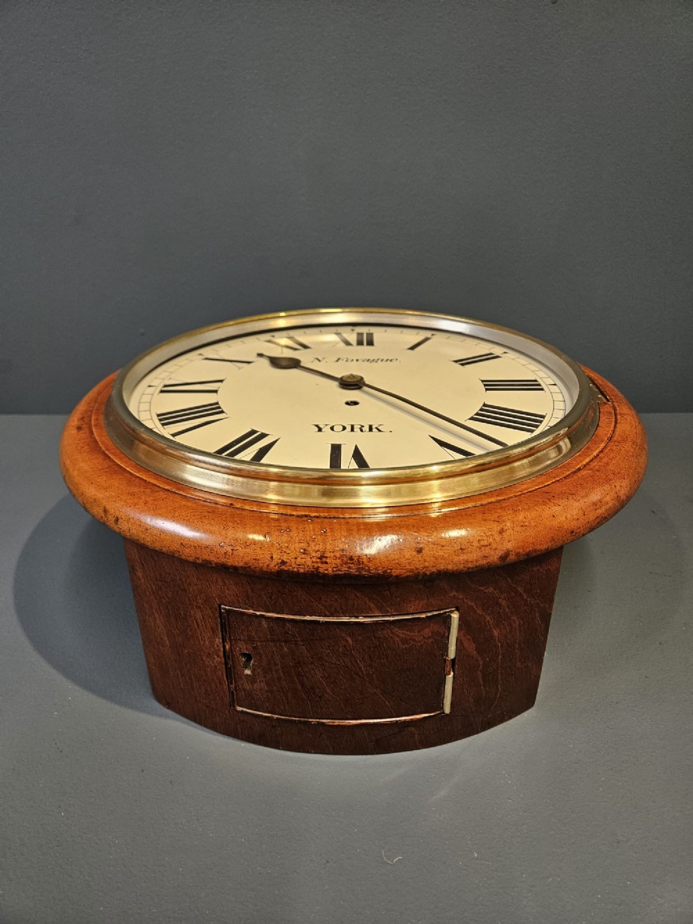 A round late Victorian mahogany wall clock featuring a brass bezel, white painted dial with black Roman numerals, and signature reading N. Fovague York. View VII