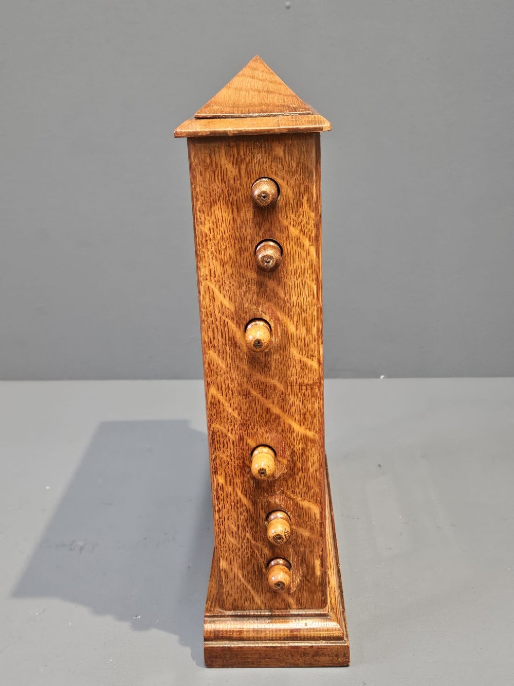 An Edwardian oak perpetual desk calendar featuring side turning knobs, apertures displaying printed day, date, and month rolls, and a gabled pediment top. View VII