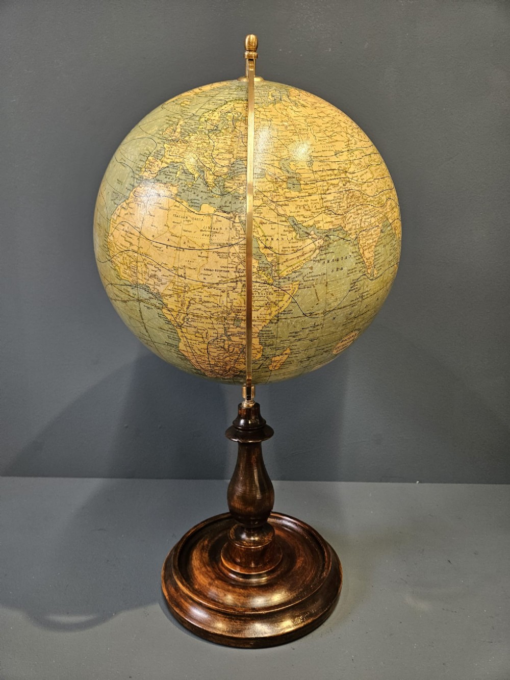 A 1920s terrestrial table globe with printed paper maps mounted on a brass semi-meridian arc and a turned dark walnut base. View XII