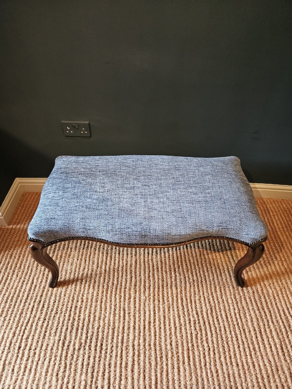 A Victorian double stool featuring dark carved wooden legs and textured light blue fabric upholstery secured with metal studding. View II
