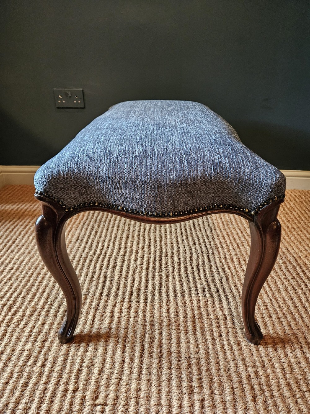 A Victorian double stool featuring dark carved wooden legs and textured light blue fabric upholstery secured with metal studding. View VI