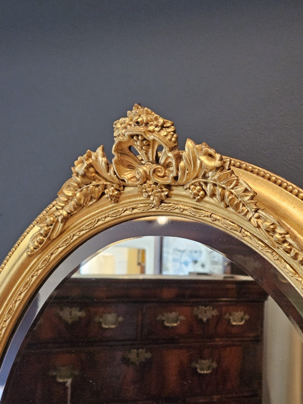 A mid-Victorian oval wall mirror featuring a giltwood frame adorned with carved cresting, beaded borders, and a bevelled mirror plate. View IV