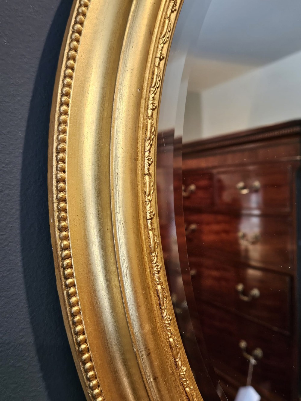 A mid-Victorian oval wall mirror featuring a giltwood frame adorned with carved cresting, beaded borders, and a bevelled mirror plate. View VI