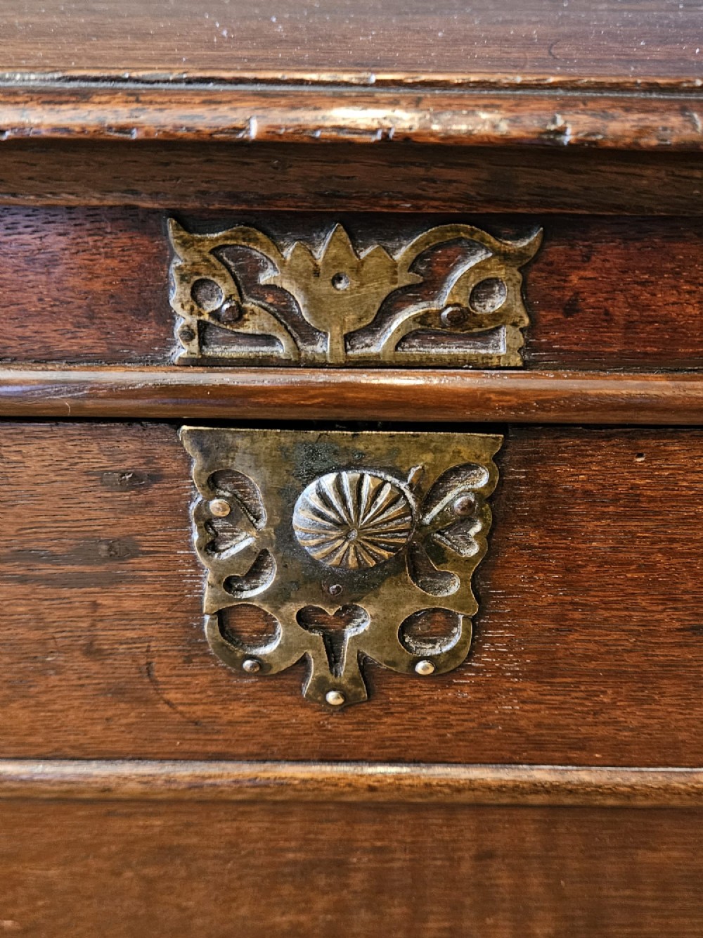 A warm brown George I oak close stool with horizontal moulded panelling, a central brass escutcheon, and turned bun feet. View II