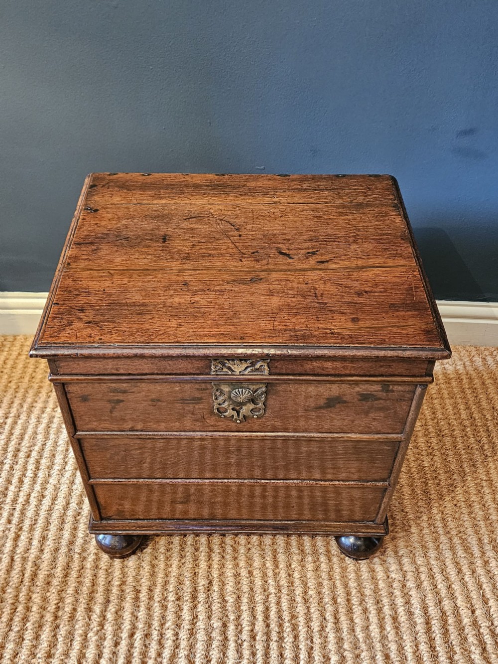A warm brown George I oak close stool with horizontal moulded panelling, a central brass escutcheon, and turned bun feet. View V