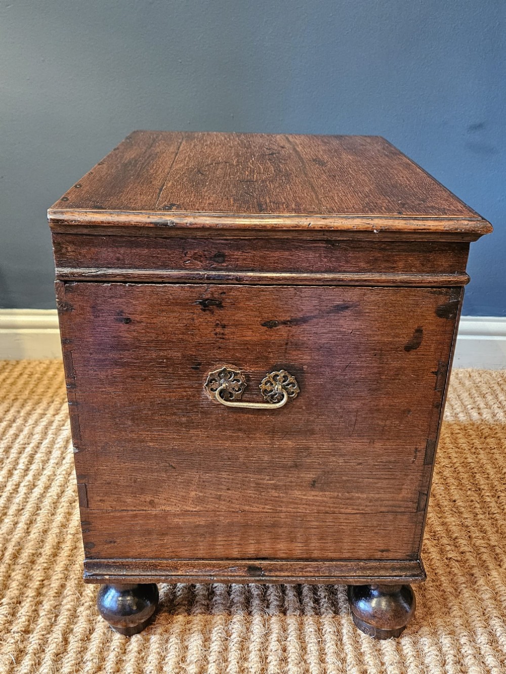 A warm brown George I oak close stool with horizontal moulded panelling, a central brass escutcheon, and turned bun feet. View VII
