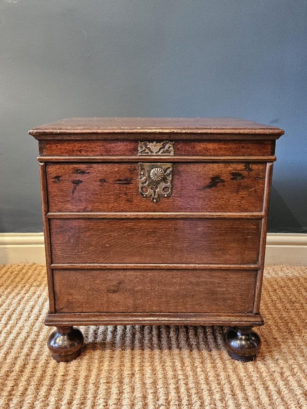 A warm brown George I oak close stool with horizontal moulded panelling, a central brass escutcheon, and turned bun feet. View VIII