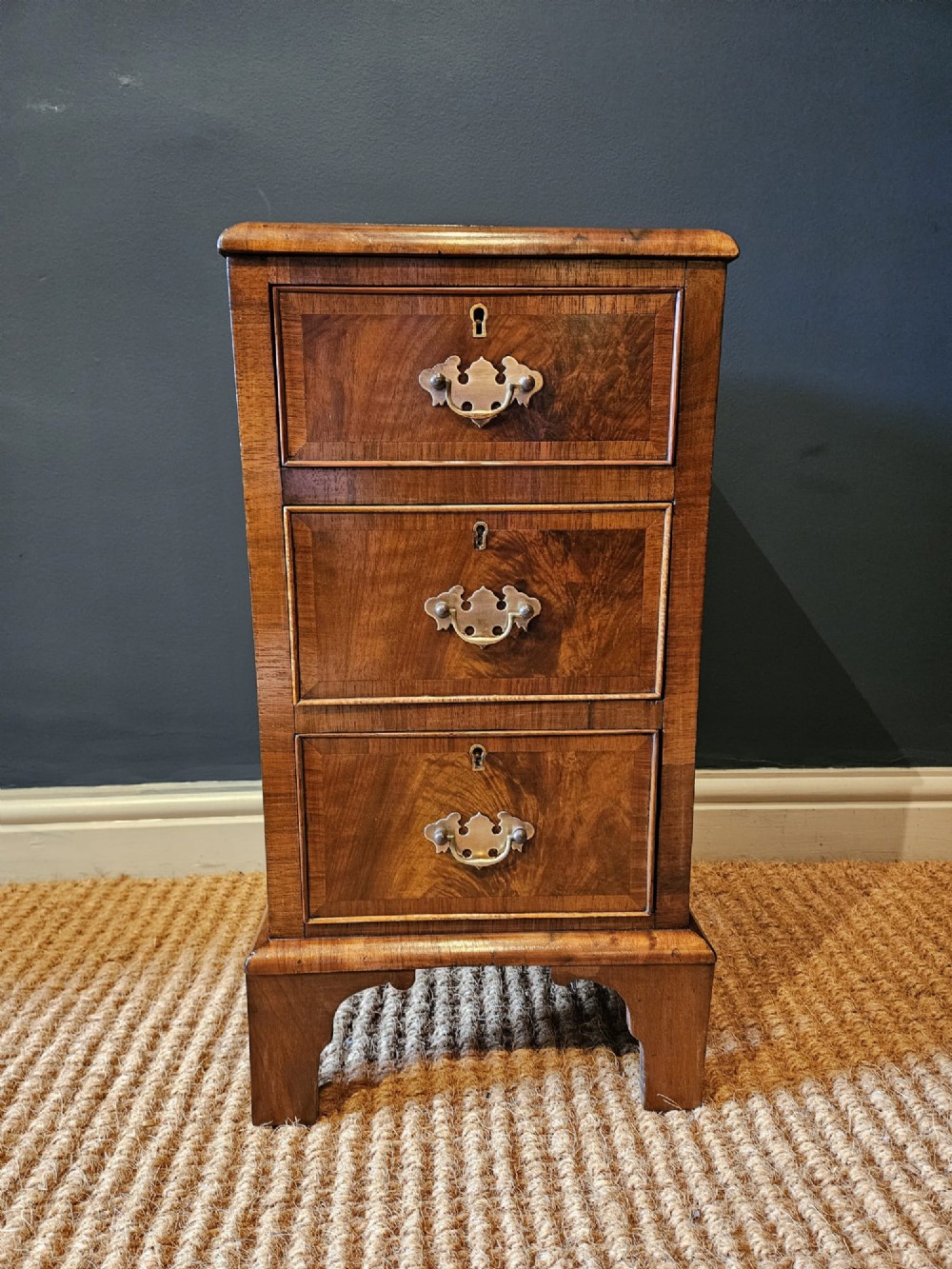 A matching pair of Victorian walnut bedside chests with three drawers, brass drop handles, and bracket feet. View V