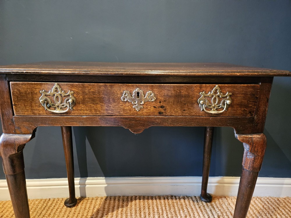 A George II dark oak side table with a single drawer, pierced brass handles, a shaped apron, and four cabriole legs terminating in pad feet. View II