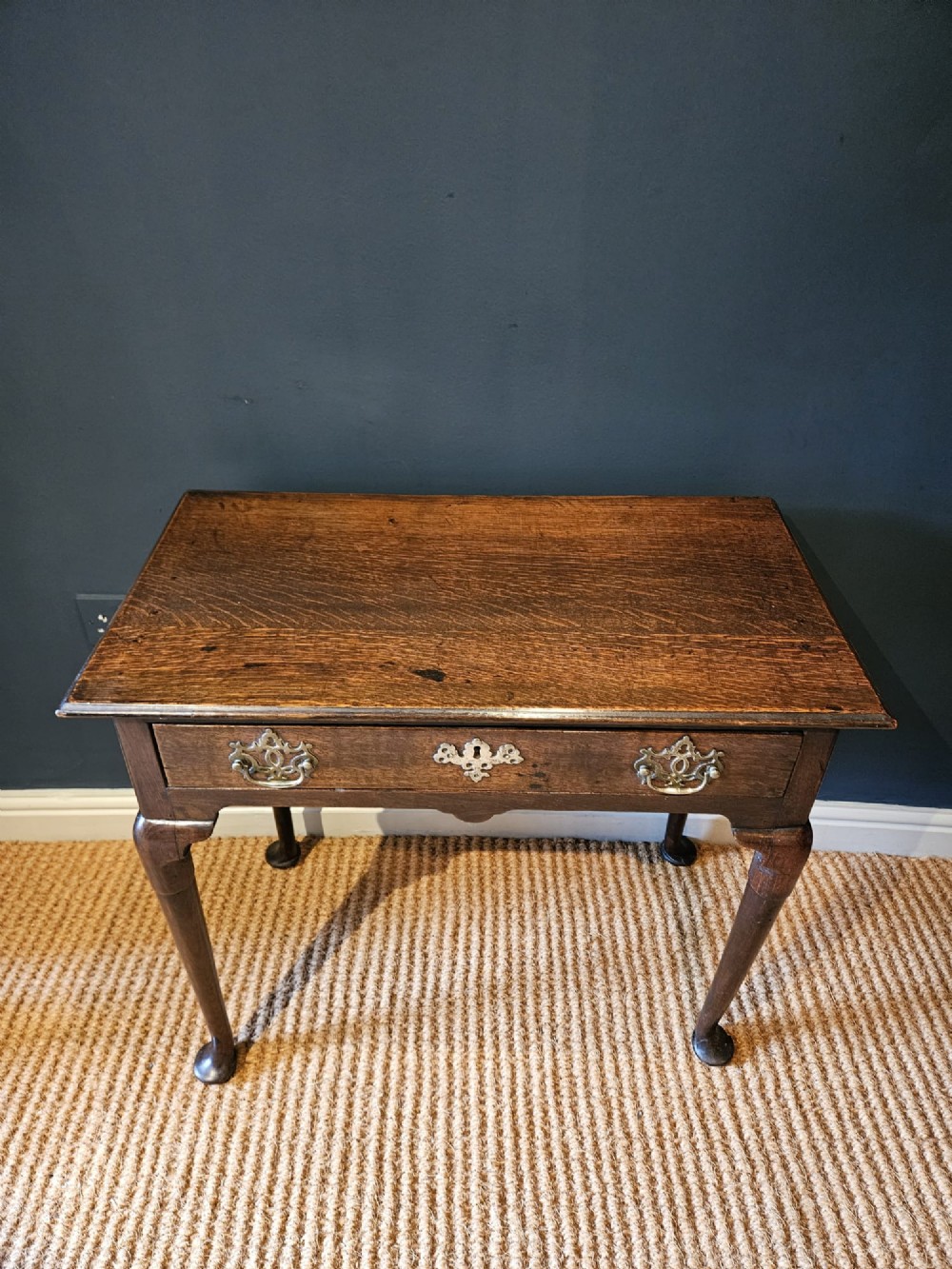 A George II dark oak side table with a single drawer, pierced brass handles, a shaped apron, and four cabriole legs terminating in pad feet. View III
