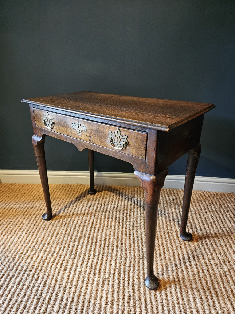 A George II dark oak side table with a single drawer, pierced brass handles, a shaped apron, and four cabriole legs terminating in pad feet. View VII