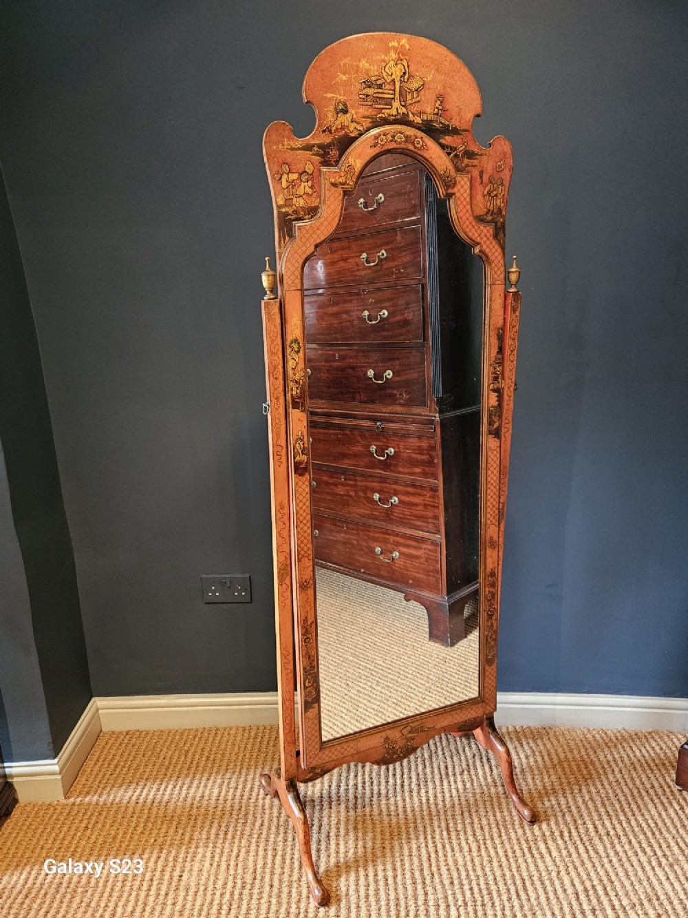 A tall 1920s Chinoiserie freestanding cheval mirror featuring an arched frame decorated with gold hand-painted Asian figures and landscapes on a warm terracotta lacquered background. View II