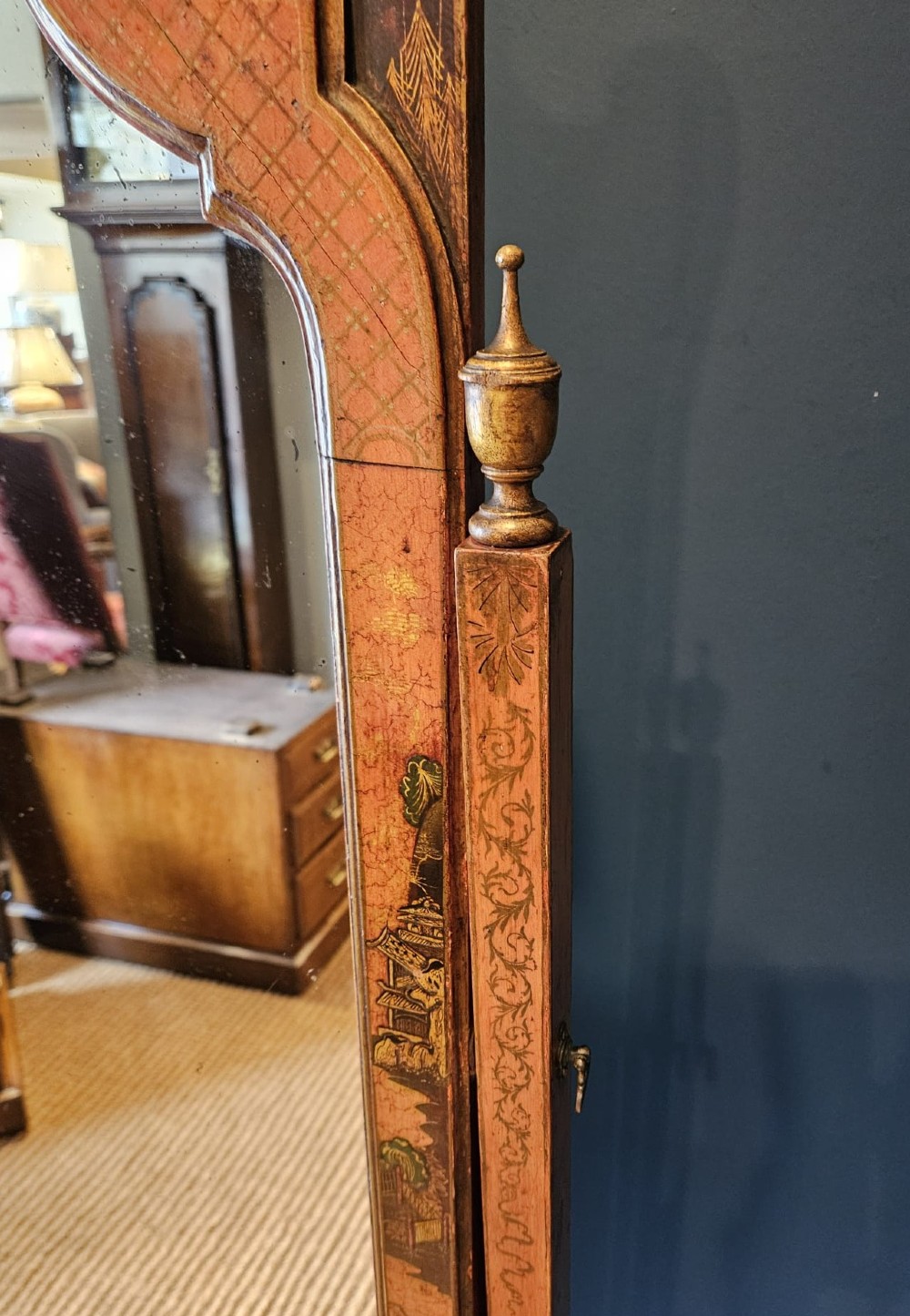 A tall 1920s Chinoiserie freestanding cheval mirror featuring an arched frame decorated with gold hand-painted Asian figures and landscapes on a warm terracotta lacquered background. View V
