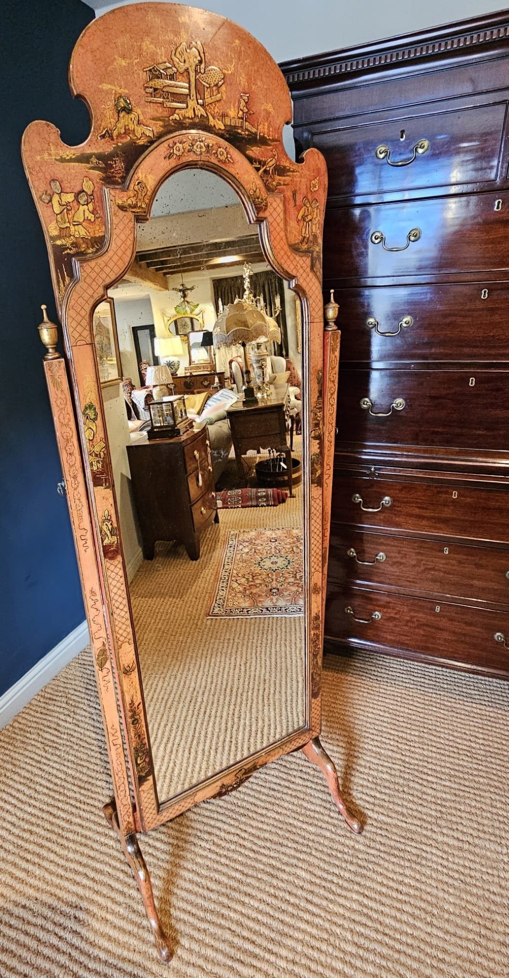 A tall 1920s Chinoiserie freestanding cheval mirror featuring an arched frame decorated with gold hand-painted Asian figures and landscapes on a warm terracotta lacquered background. View X