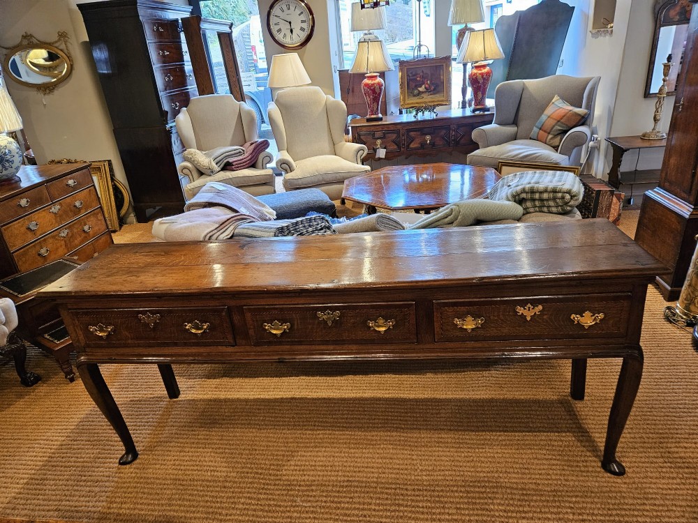 A mid-18th century George II dark oak dresser base featuring three drawers with brass swan-neck handles, raised on slender cabriole legs with pad feet. View IX