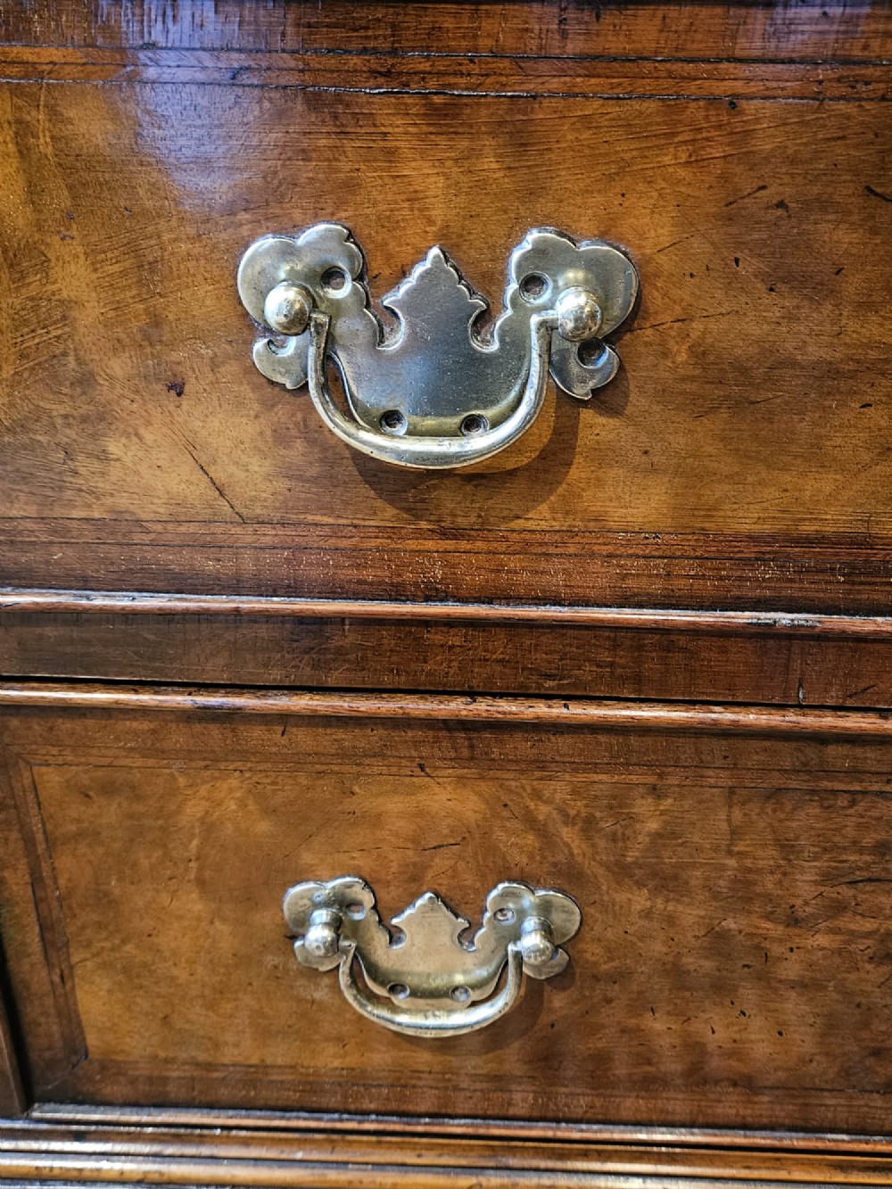 A small George III walnut chest of drawers featuring four graduated drawers with brass handles, keyhole escutcheons, and bracket feet against a dark grey background. View II