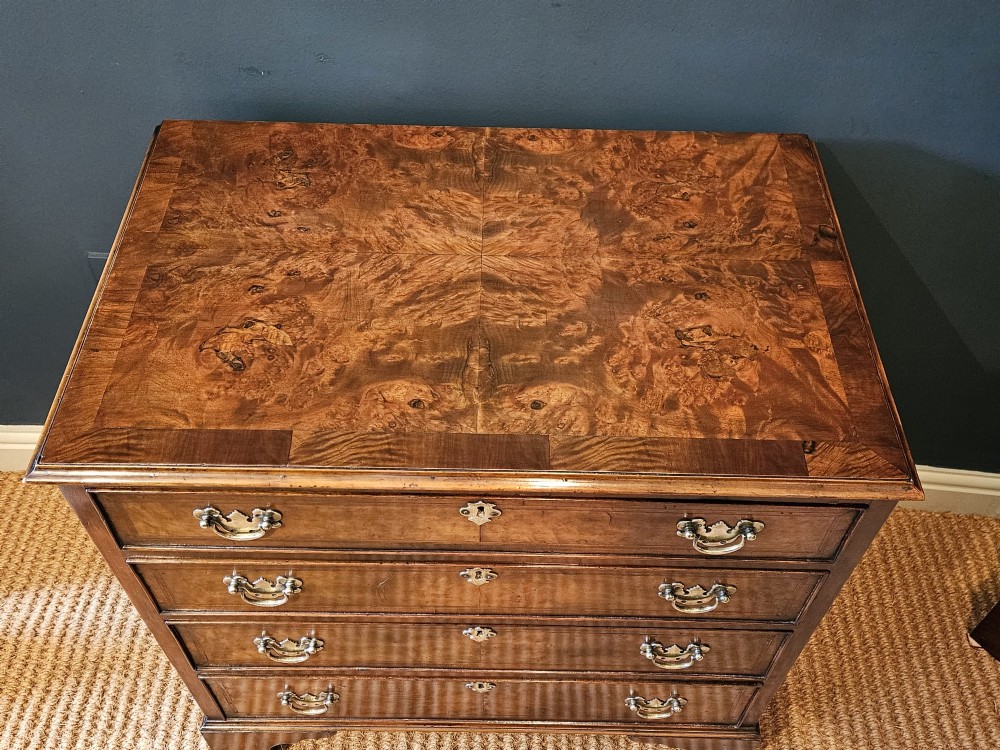 A small George III walnut chest of drawers featuring four graduated drawers with brass handles, keyhole escutcheons, and bracket feet against a dark grey background. View VI