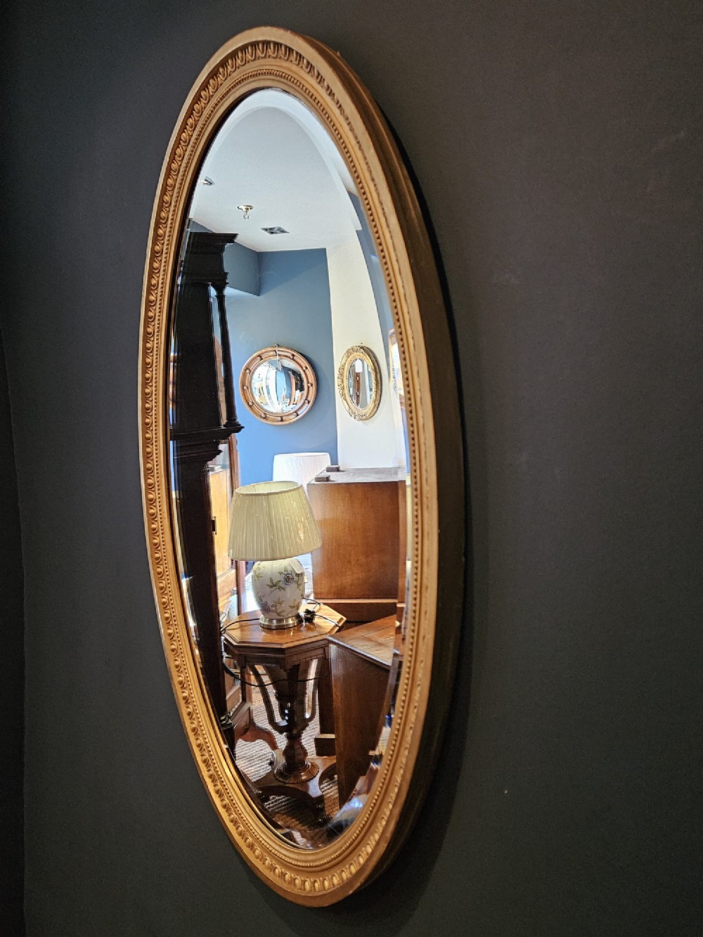 A vertical oval wall mirror featuring a gilded plaster frame decorated with egg and dart moulding details around the inner border. View IV