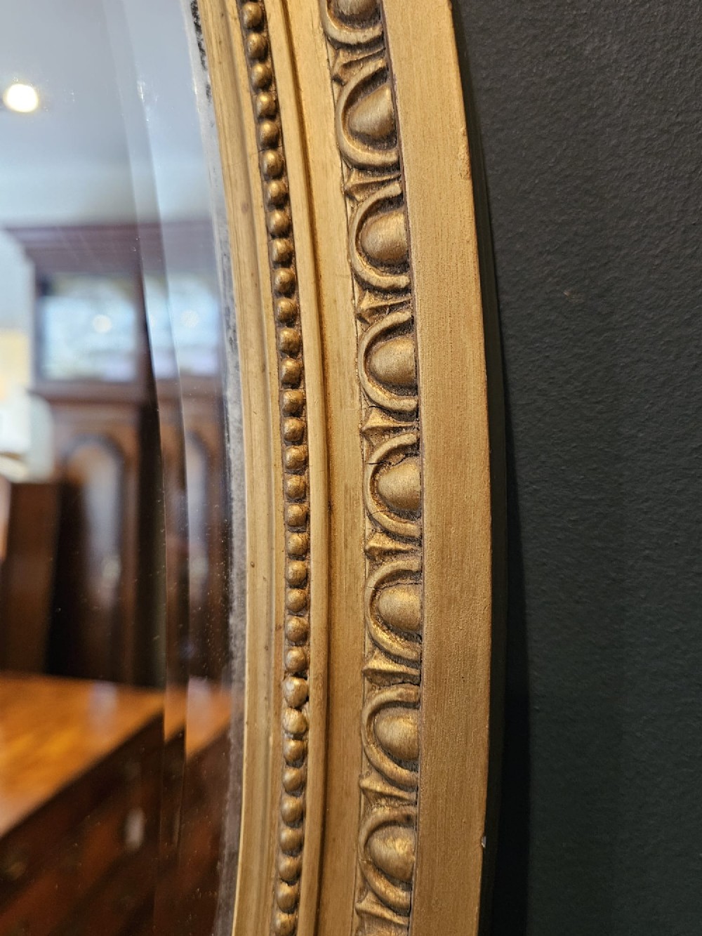A vertical oval wall mirror featuring a gilded plaster frame decorated with egg and dart moulding details around the inner border. View V