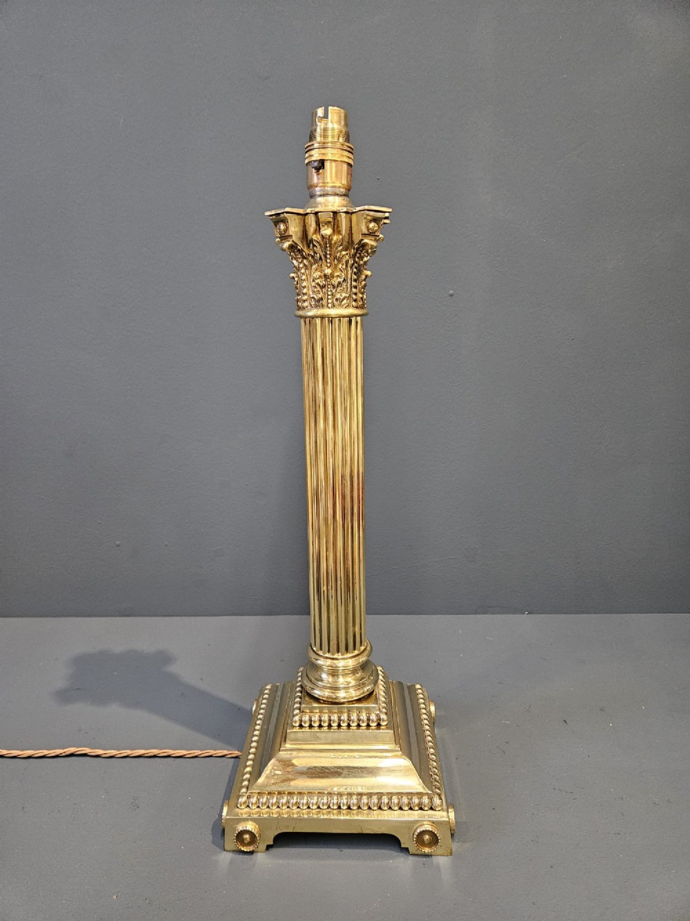 An antique brass table lamp designed as a fluted Corinthian column on a square stepped base with beaded detailing.