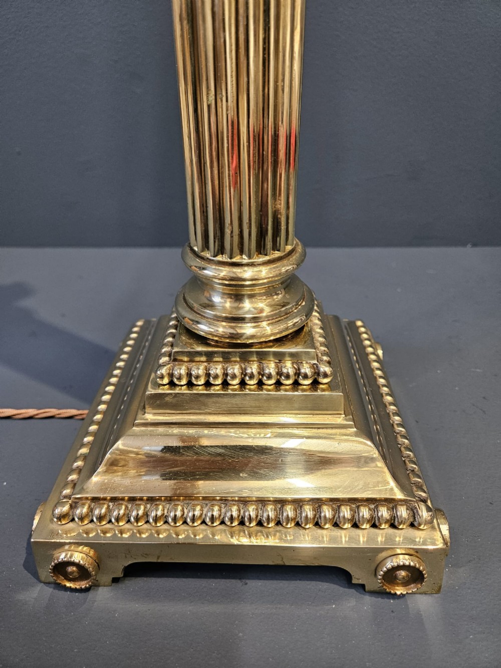 An antique brass table lamp designed as a fluted Corinthian column on a square stepped base with beaded detailing. View II