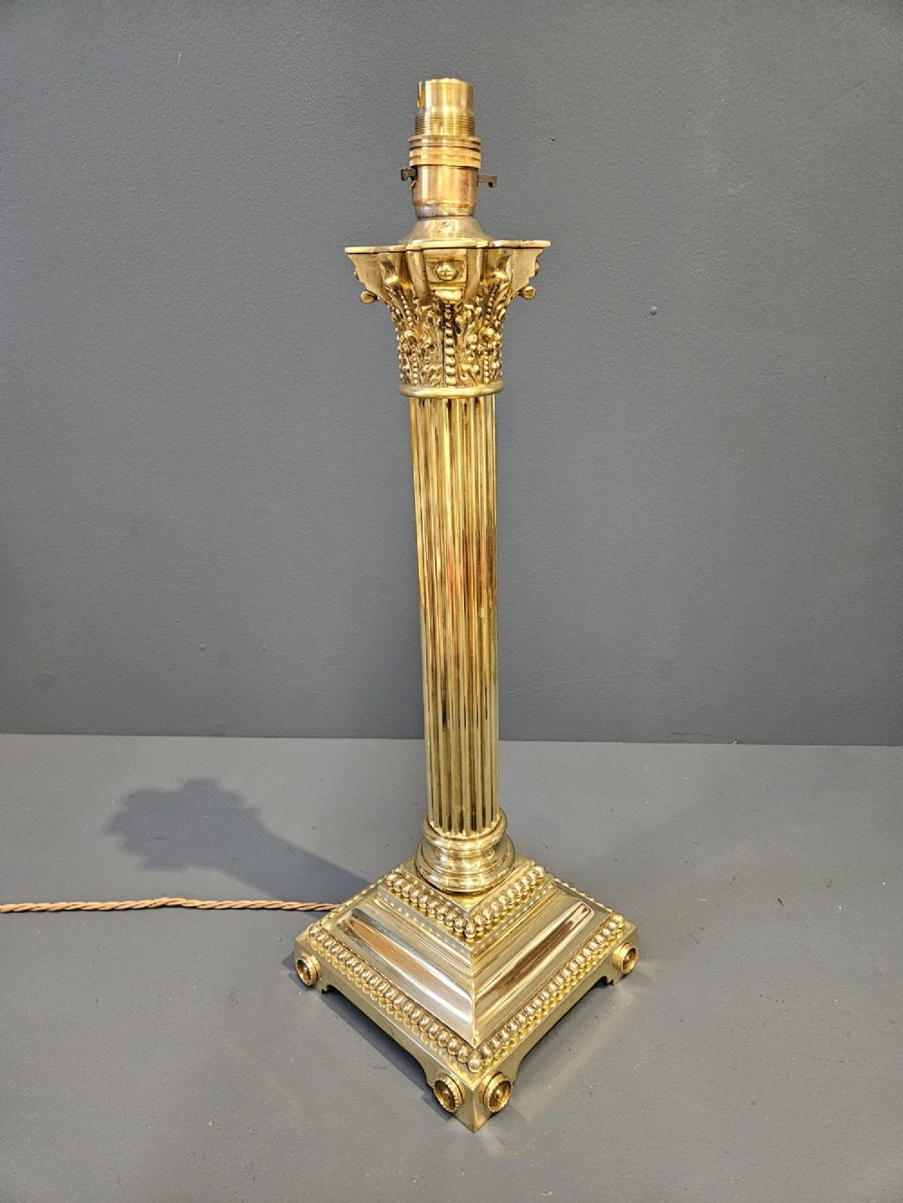 An antique brass table lamp designed as a fluted Corinthian column on a square stepped base with beaded detailing. View V