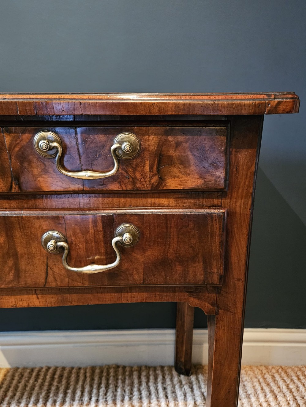 A Georgian walnut side table featuring three drawers with brass handles and straight legs set against a dark blue wall. View III