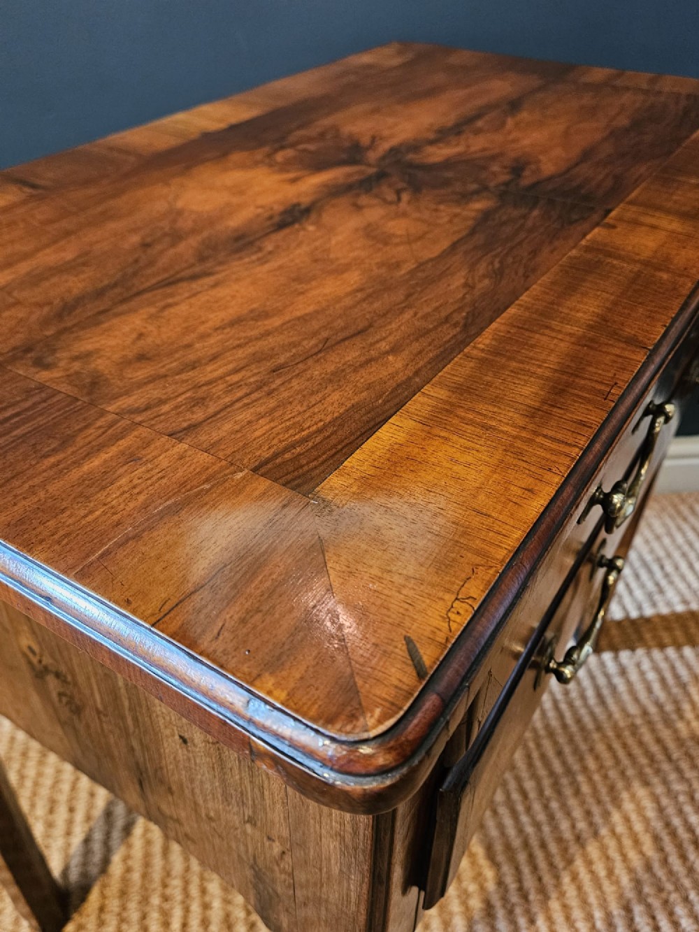 A Georgian walnut side table featuring three drawers with brass handles and straight legs set against a dark blue wall. View V