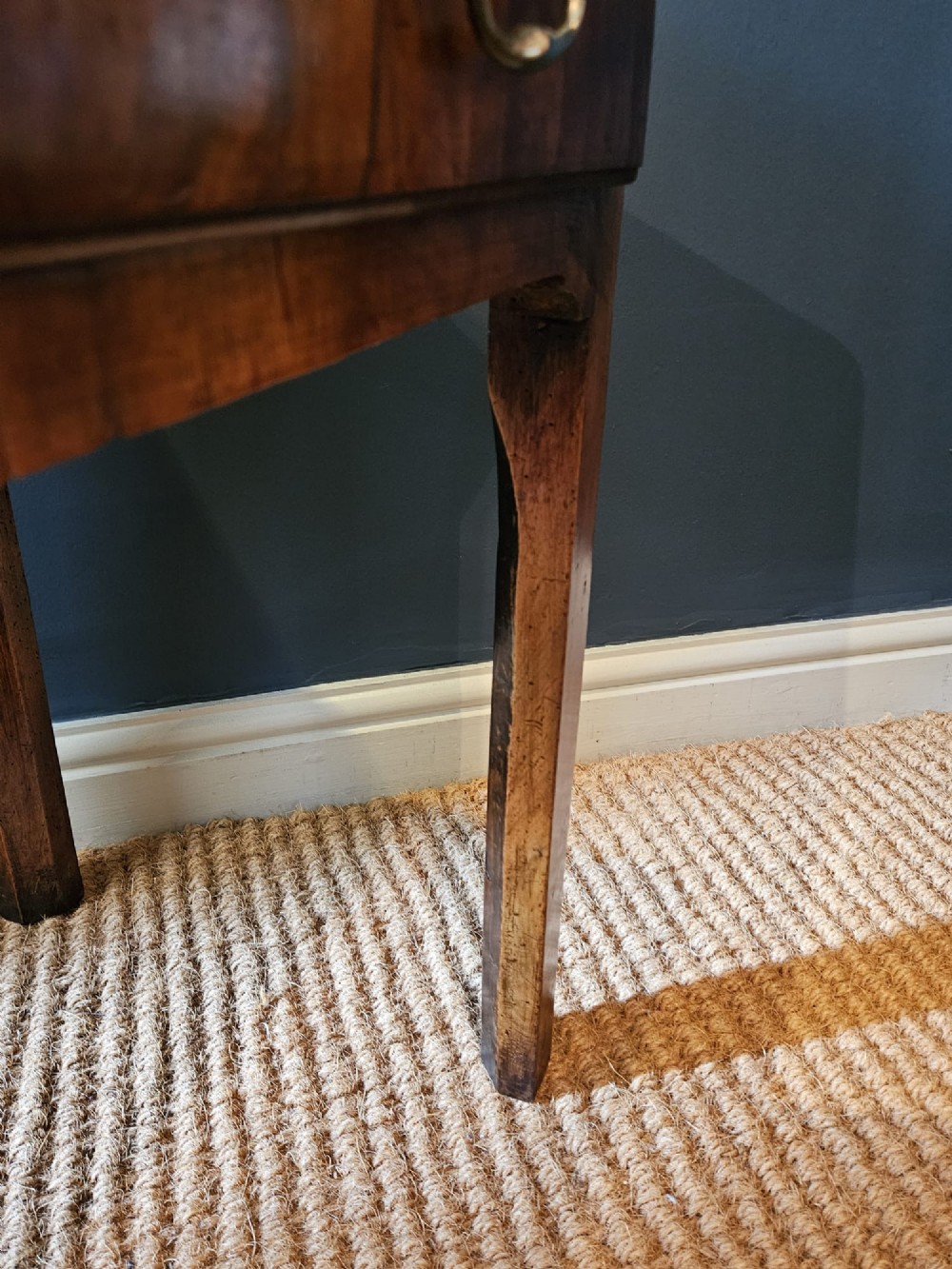 A Georgian walnut side table featuring three drawers with brass handles and straight legs set against a dark blue wall. View VII
