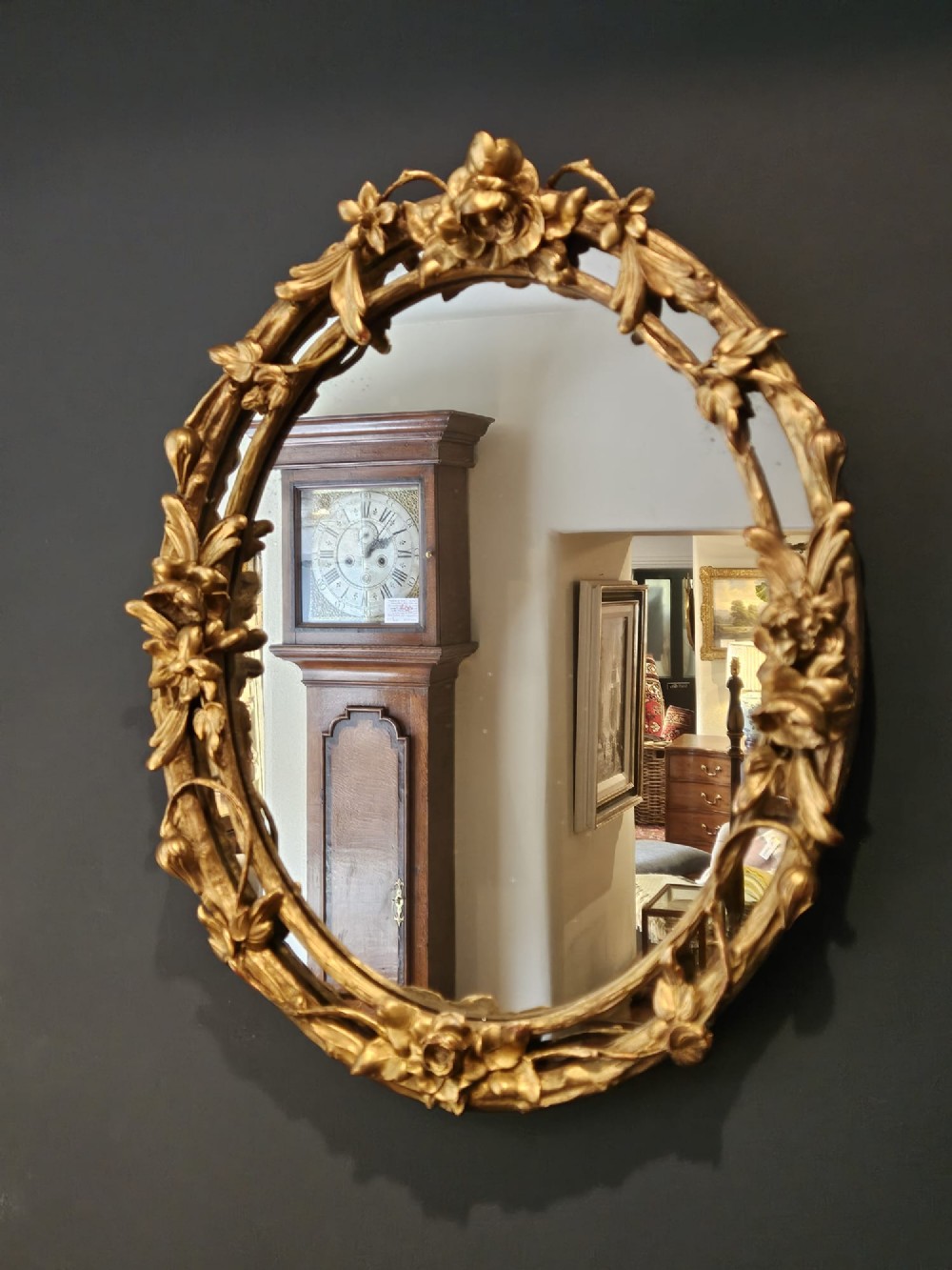 An oval Victorian giltwood wall mirror featuring a frame intricately carved with rose blossoms, foliage, and vine motifs. View II