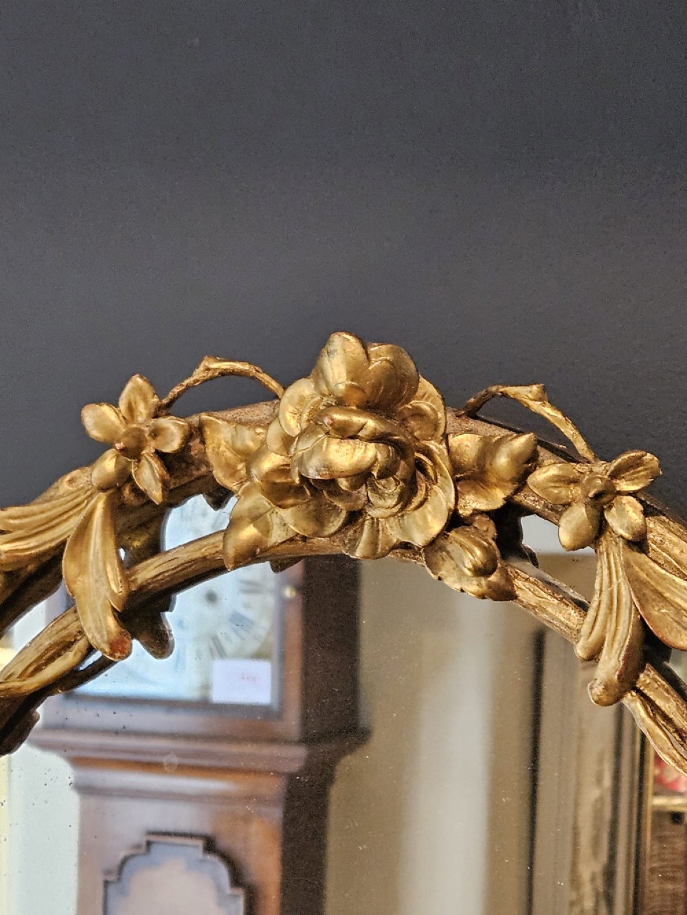 An oval Victorian giltwood wall mirror featuring a frame intricately carved with rose blossoms, foliage, and vine motifs. View V